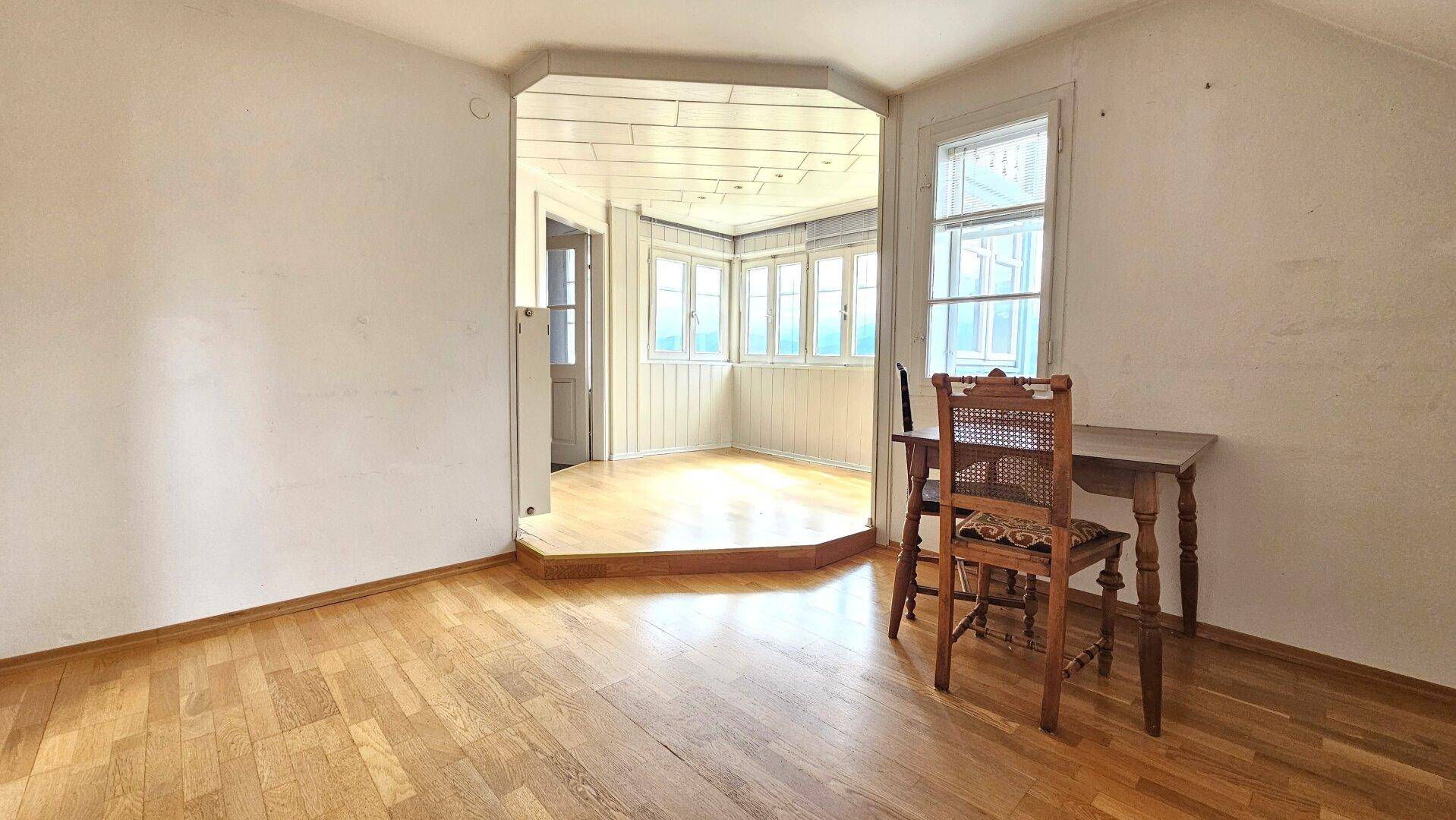Heller Raum mit Holzboden und einem Erkerbereich, der viel Tageslicht hereinlässt.