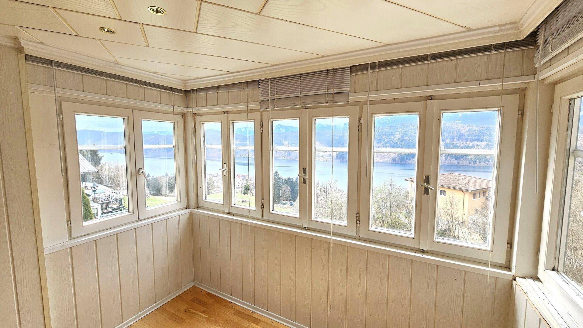 Lichtdurchfluteter Erkerbereich mit Holzboden und Panoramafenstern, die einen weiten Seeblick bieten.