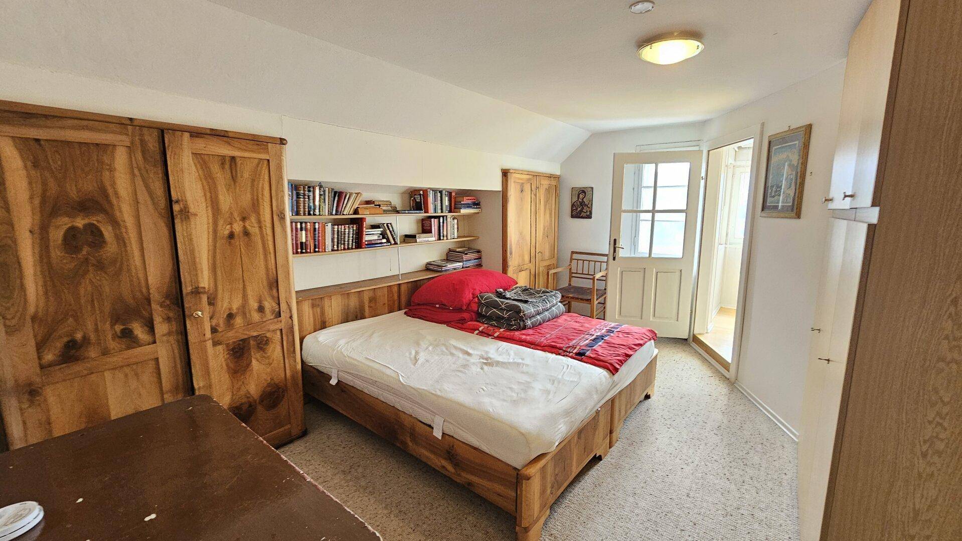 Schlafzimmer mit Holzbett, Kleiderschrank und Zugang zu einem Balkon oder einer Terrasse.