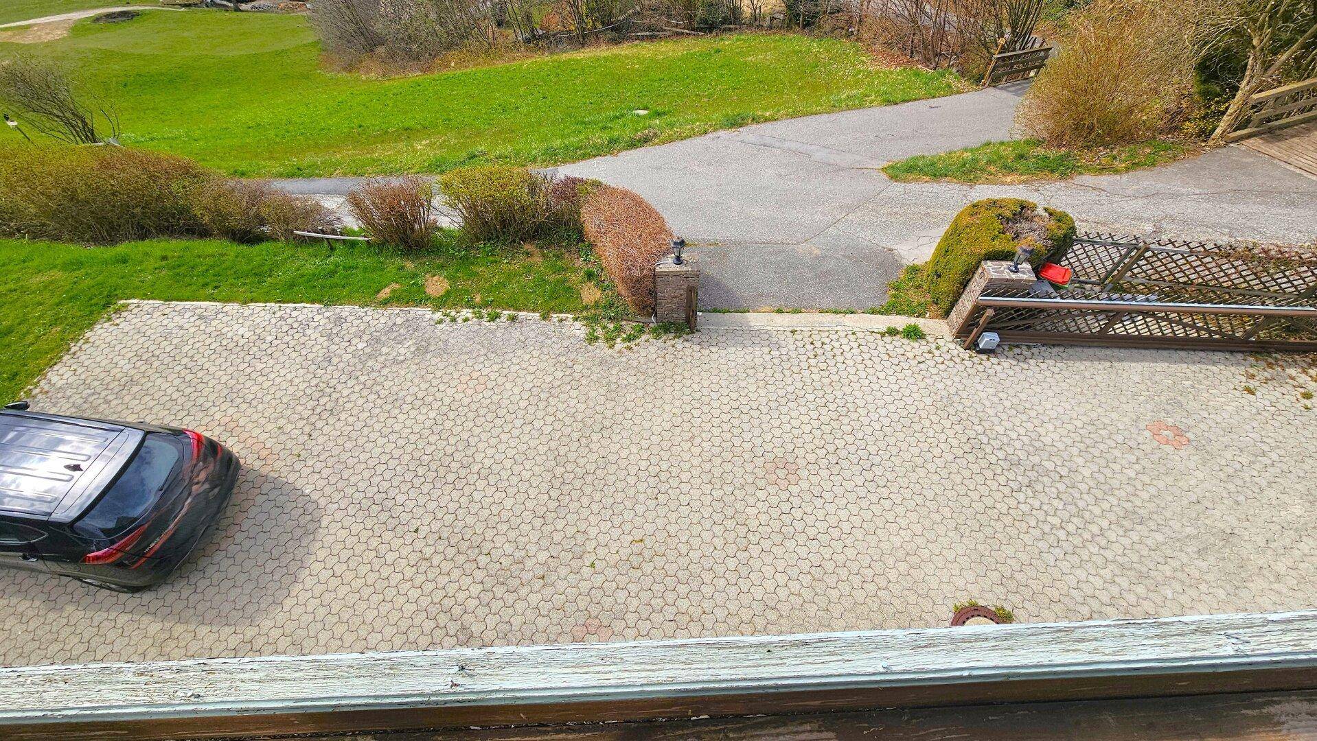 Gepflasterte Auffahrt mit einem geparkten Auto und Blick auf die umliegende Landschaft.
