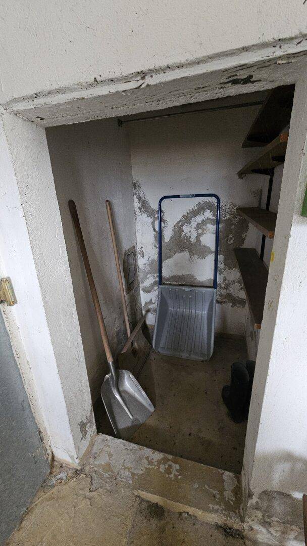 Kleine Abstellnische im Keller mit Schaufeln und Regalen für Werkzeuge und Vorräte.