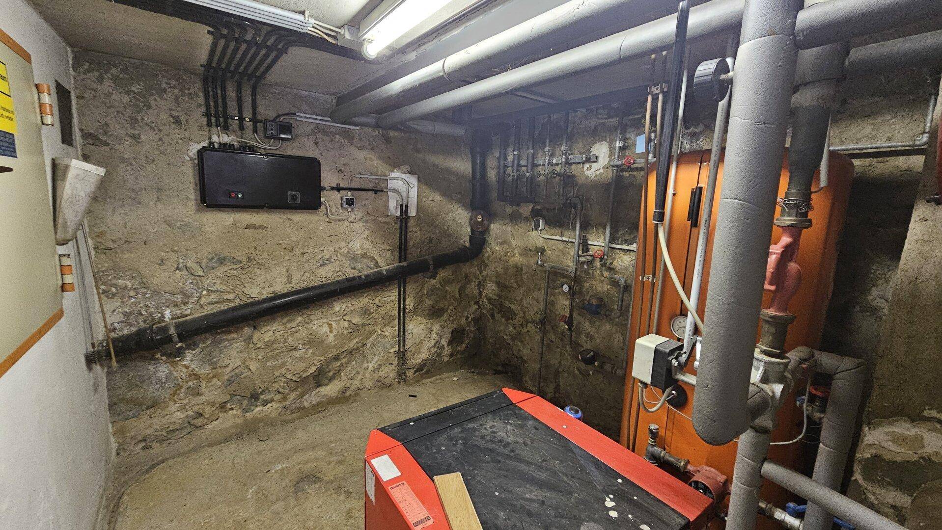 Kellerraum mit Heizungsanlage, Rohren und Leitungen, der als Technikraum dient.