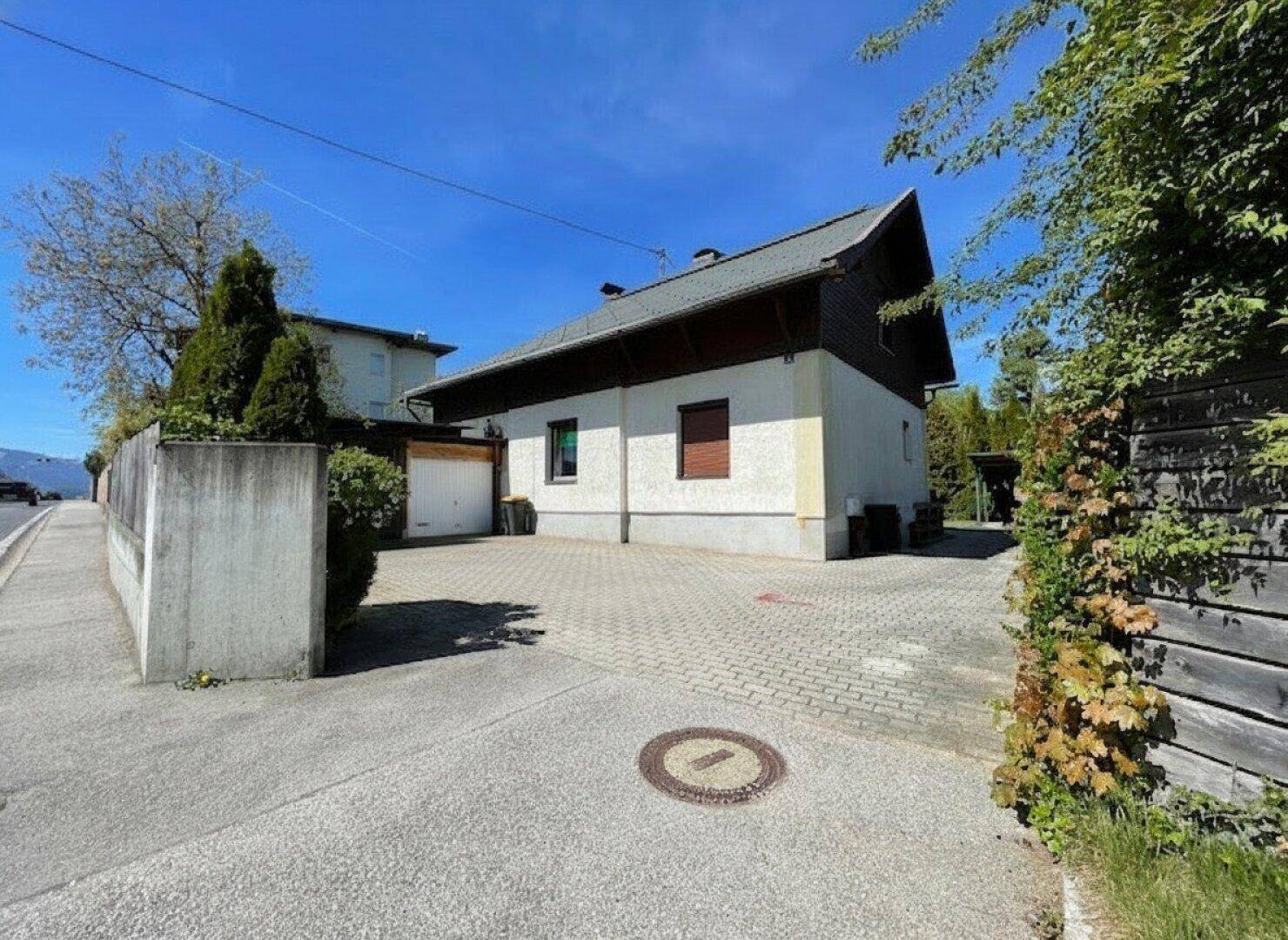 Seitenansicht des Hauses mit gepflasterter Einfahrt und Garage unter strahlend blauem Himmel.