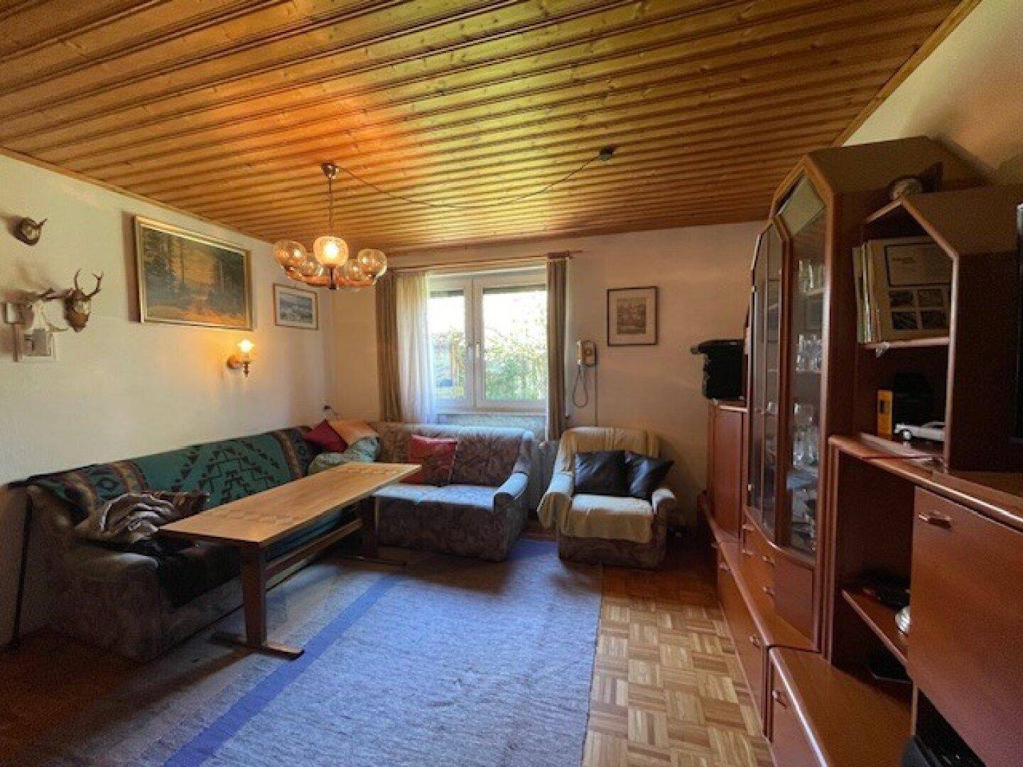 Traditionelles Wohnzimmer mit Holzdecke, gemütlicher Sitzecke und rustikalen Hirschgeweih-Dekorationen.