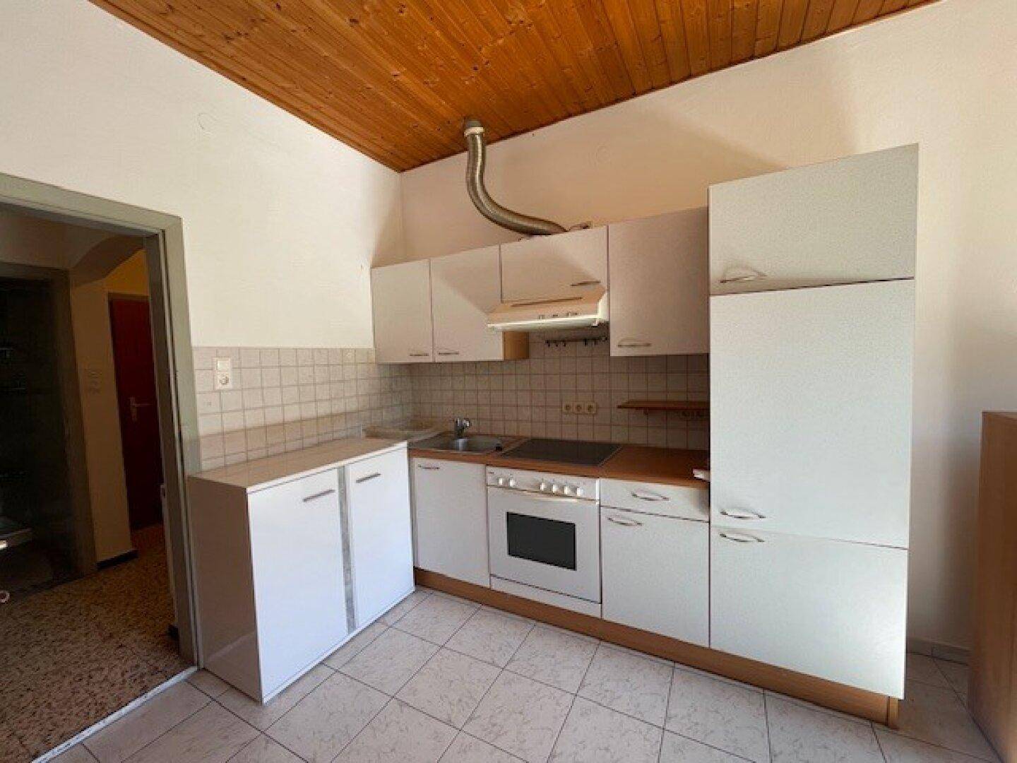 Funktionale Küche mit weißen Einbauschränken, integriertem Backofen und gefliestem Boden.