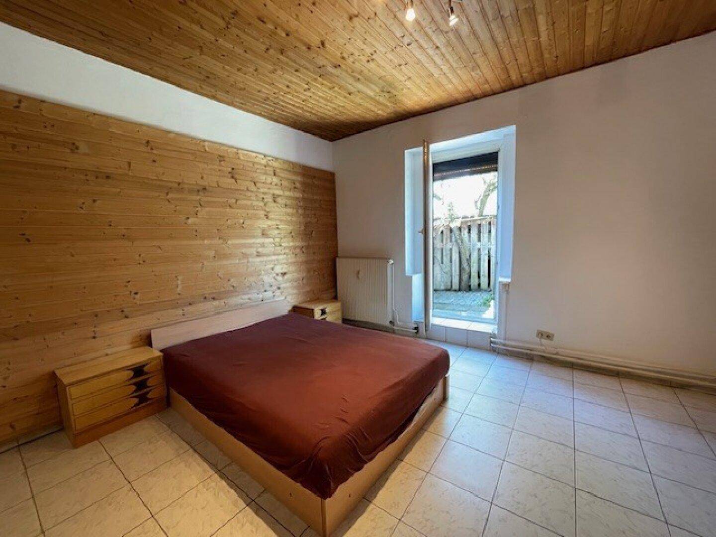 Schlafzimmer mit gefliestem Boden, Holzwand und direktem Zugang zu einem kleinen Außenbereich.