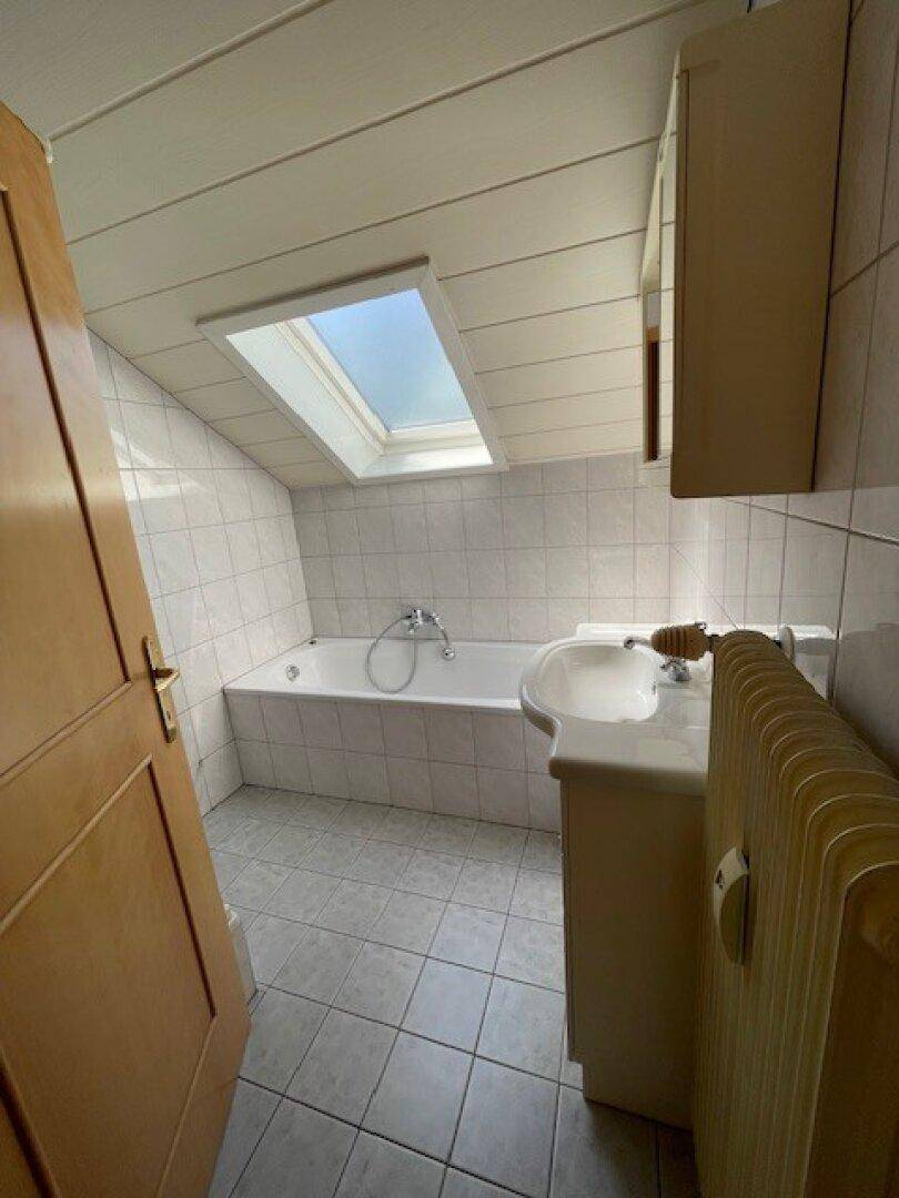 Badezimmer mit Badewanne, Waschbecken und Dachfenster, das für natürliches Licht sorgt.