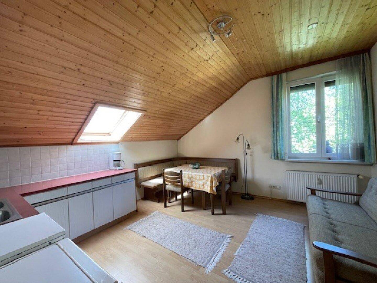 Offener Wohn- und Essbereich im Dachgeschoss mit Holzdecke, Dachfenster und kleiner Küchenzeile.