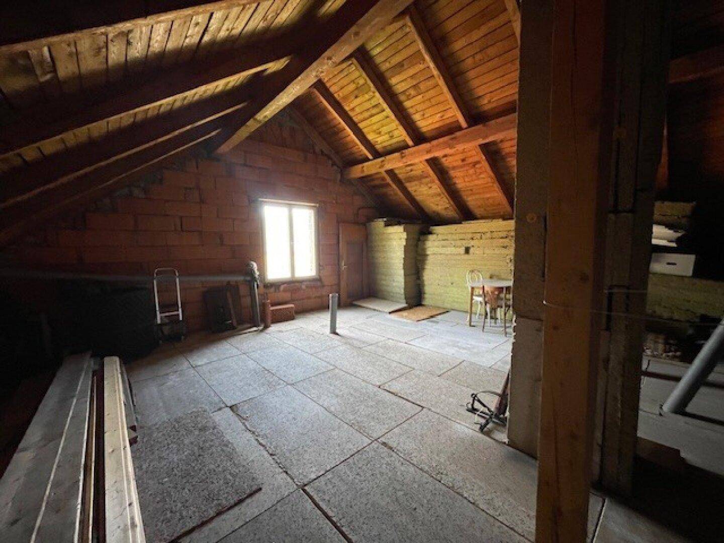 Geräumiger, unausgebauter Dachboden mit sichtbaren Holzbalken und einem Fenster.