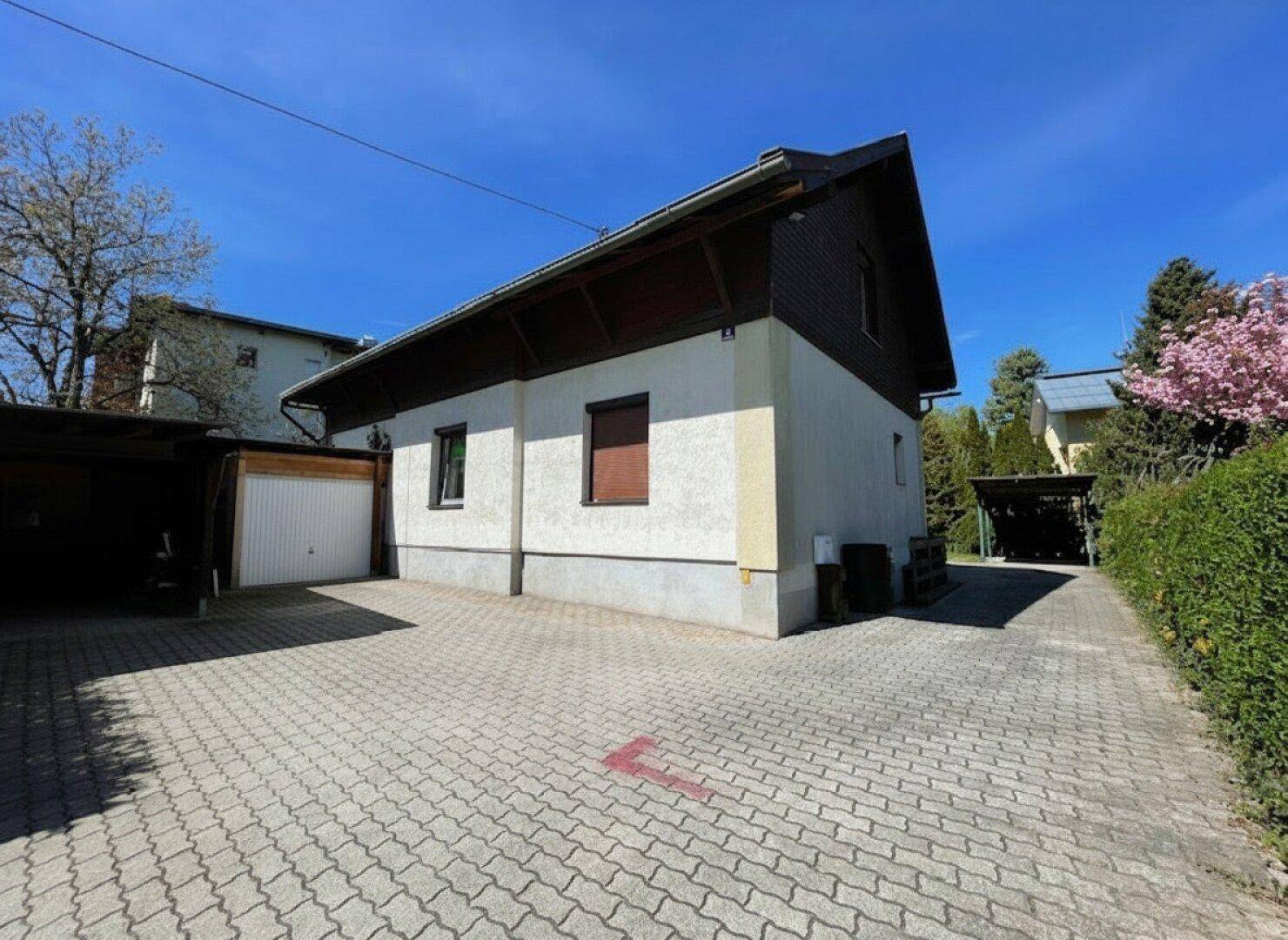 Seitenansicht des Hauses mit gepflasterter Einfahrt, Garage und Carport im Hintergrund.