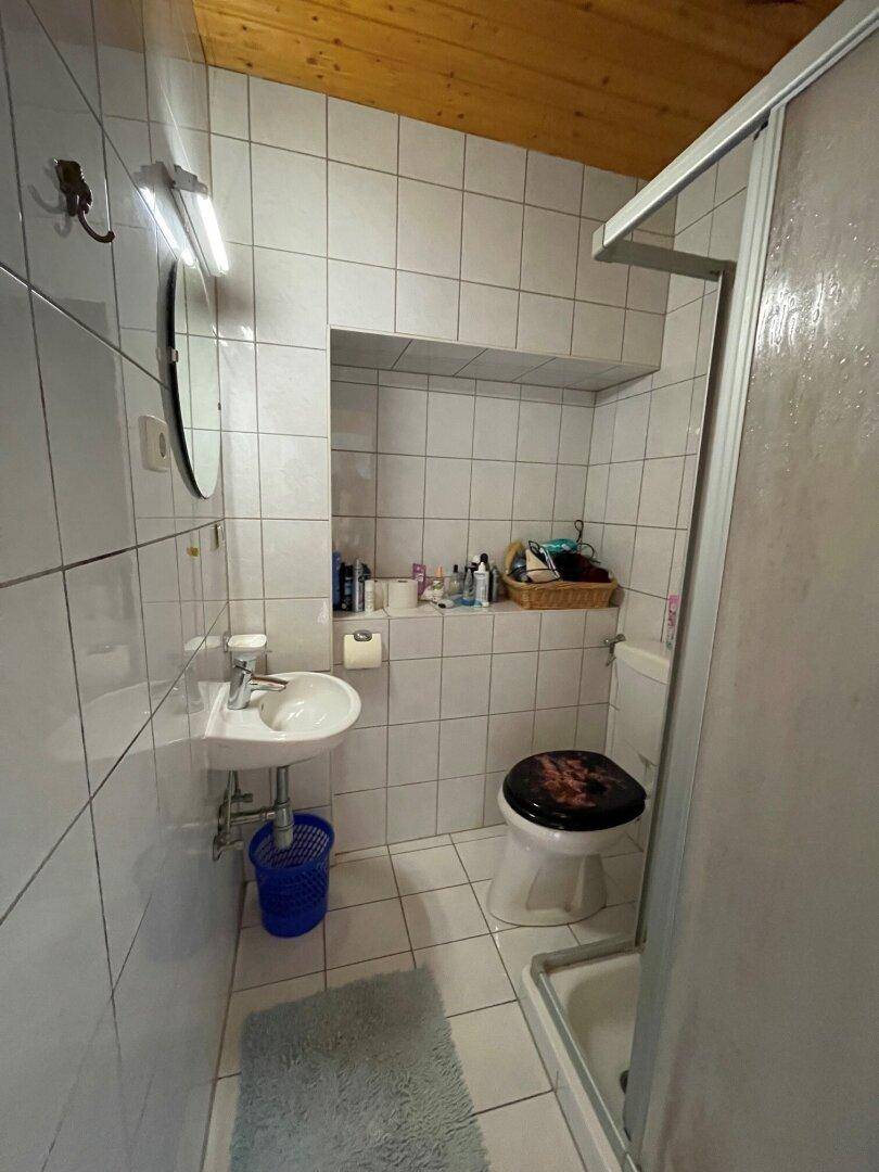 Kleines Badezimmer mit weißen Fliesen, Waschbecken, Toilette und Duschkabine.