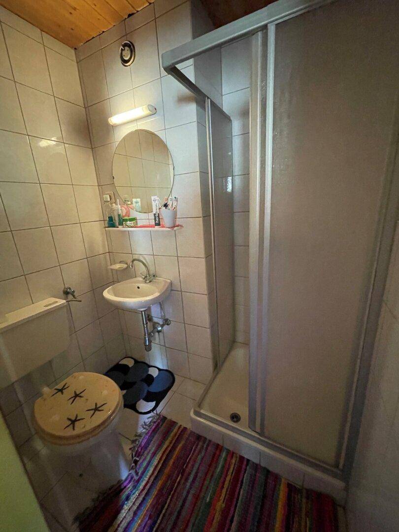 Badezimmer mit weißen Fliesen, Waschbecken, Toilette und Duschkabine.