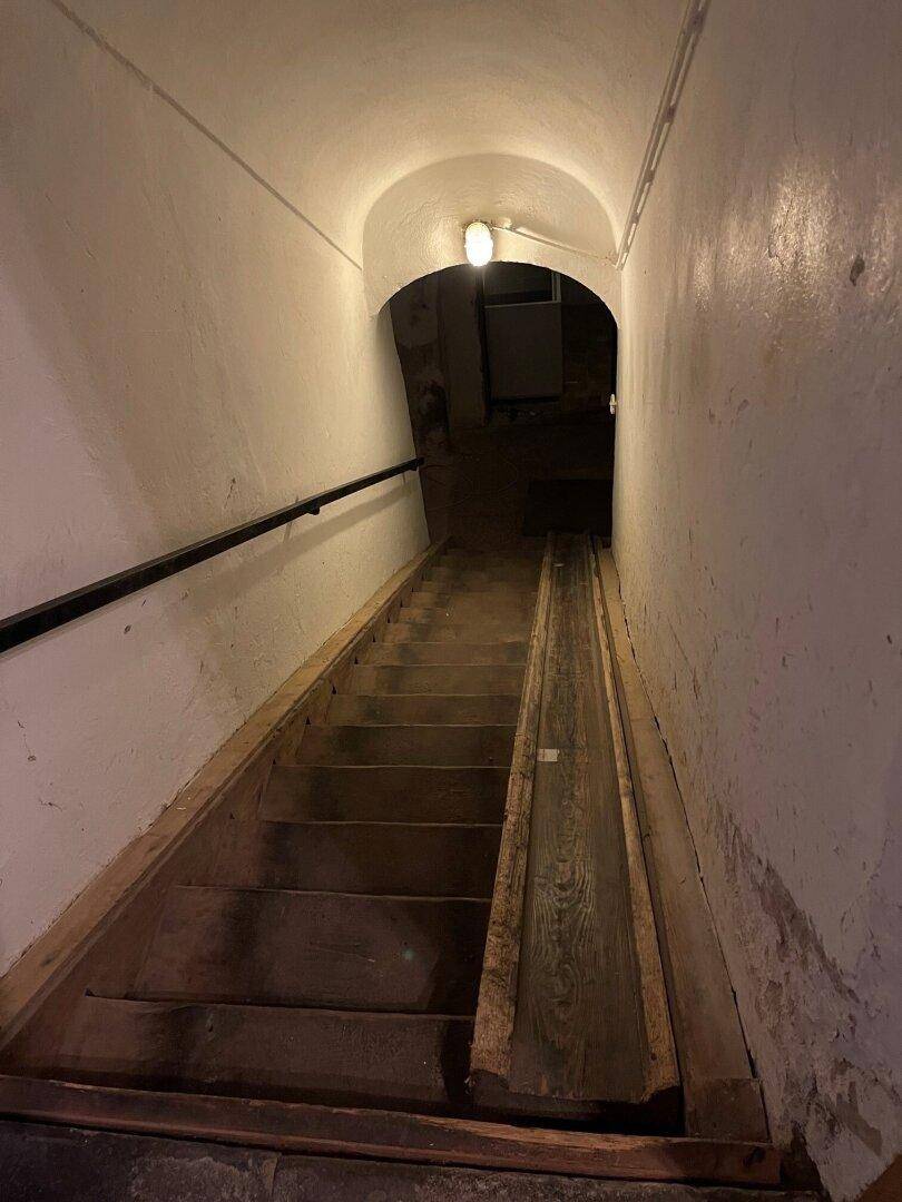 Kellerabgang mit Holztreppe, Handlauf und gewölbter Decke.