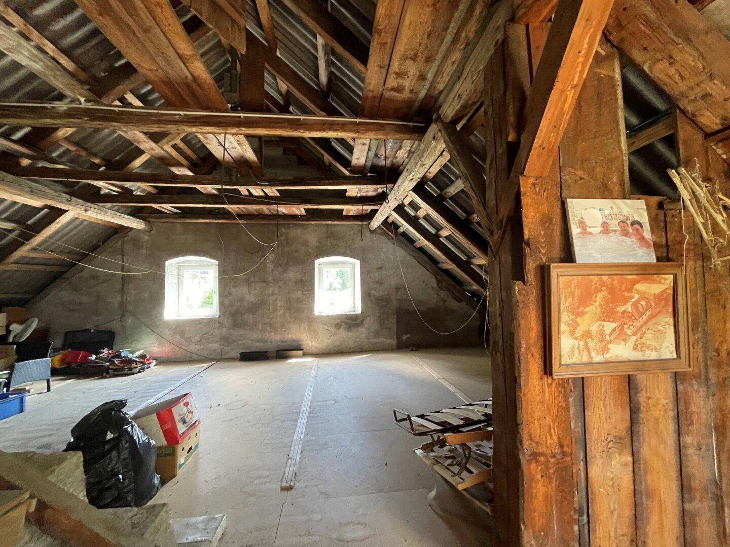 Geräumiger Dachboden mit sichtbaren Holzbalken und zwei kleinen Fenstern.