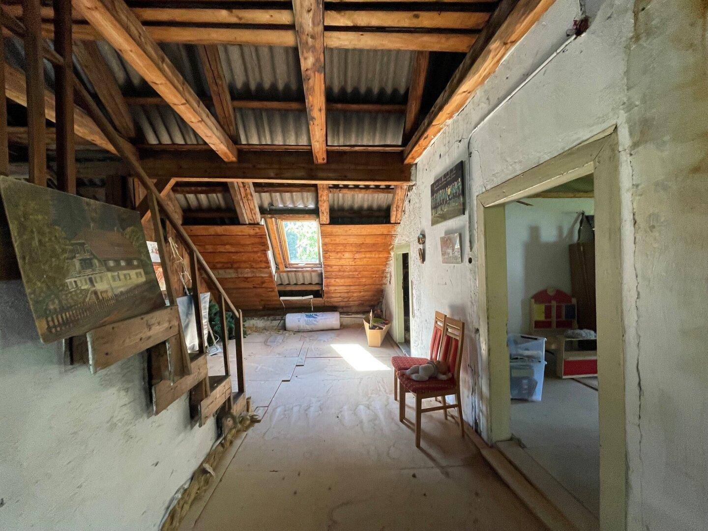 Dachbodenflur mit Holztreppe, sichtbaren Balken und einem Dachfenster.