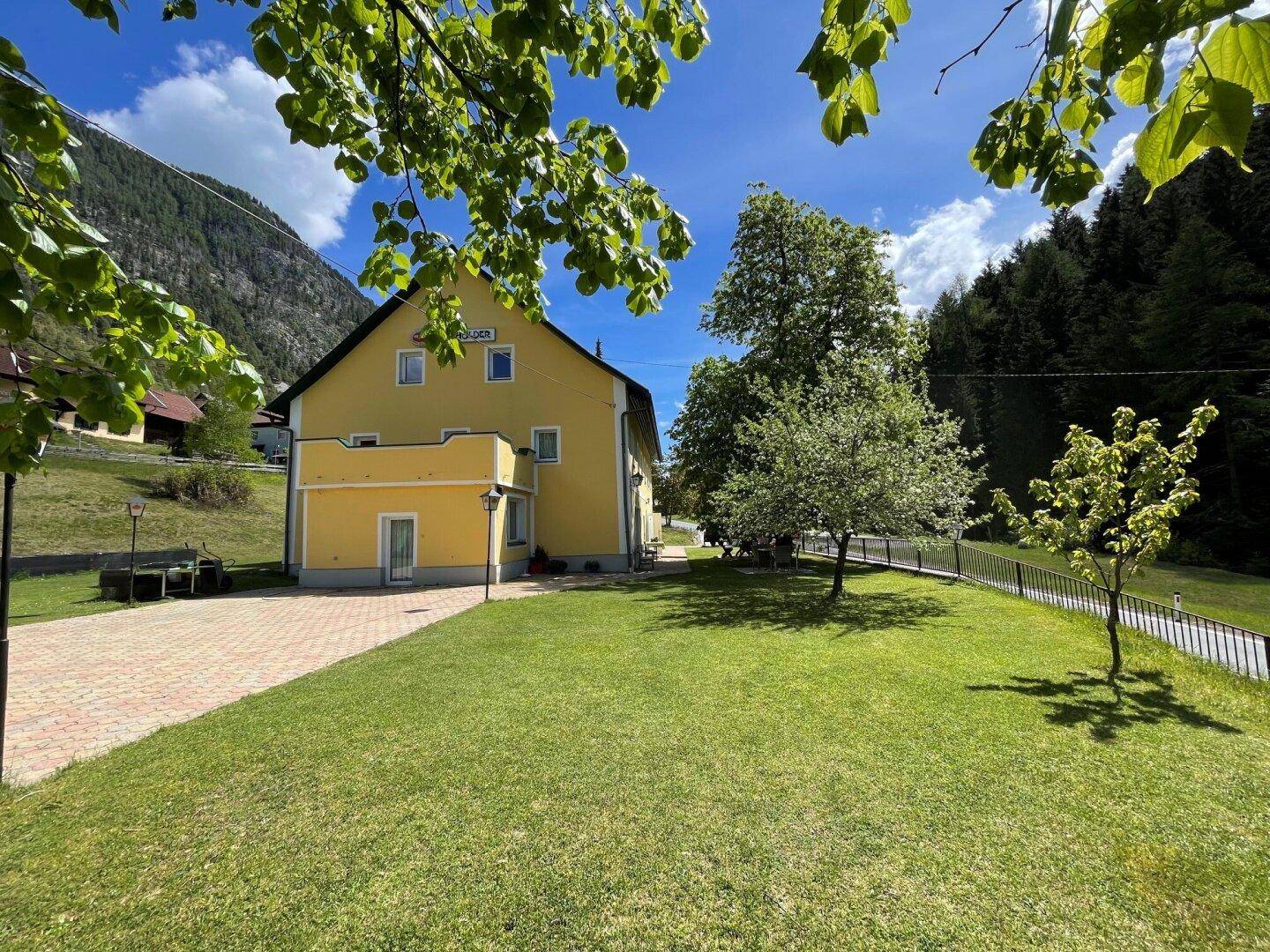 Weitläufiger Garten mit Rasenfläche, Bäumen und Blick auf das gelbe Gebäude.
