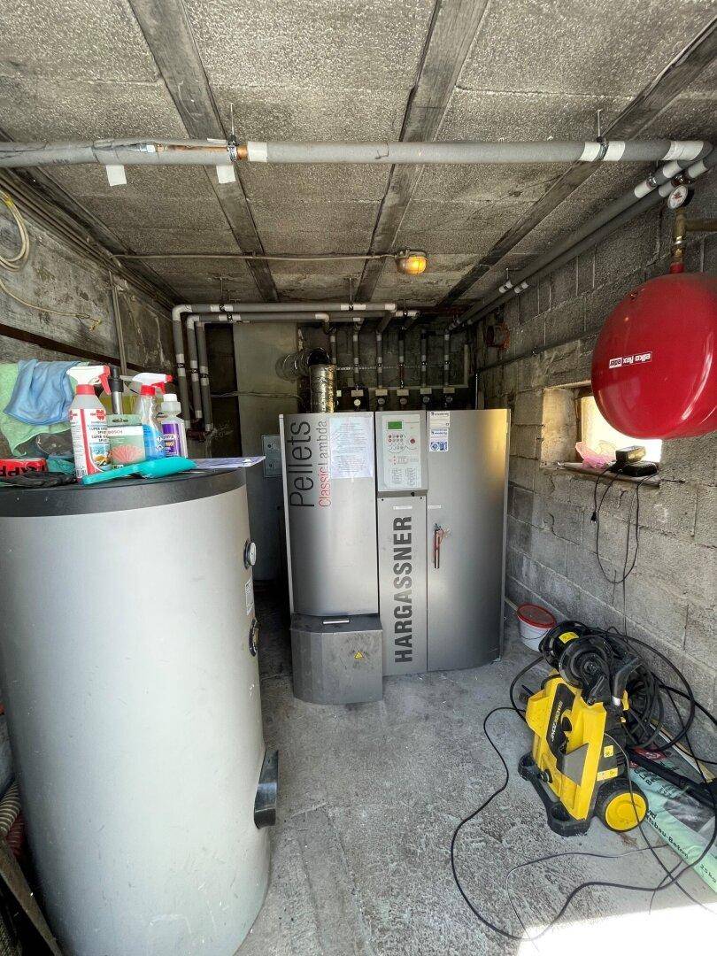 Heizungsraum mit Pelletkessel, Warmwasserspeicher und freiliegenden Rohren.
