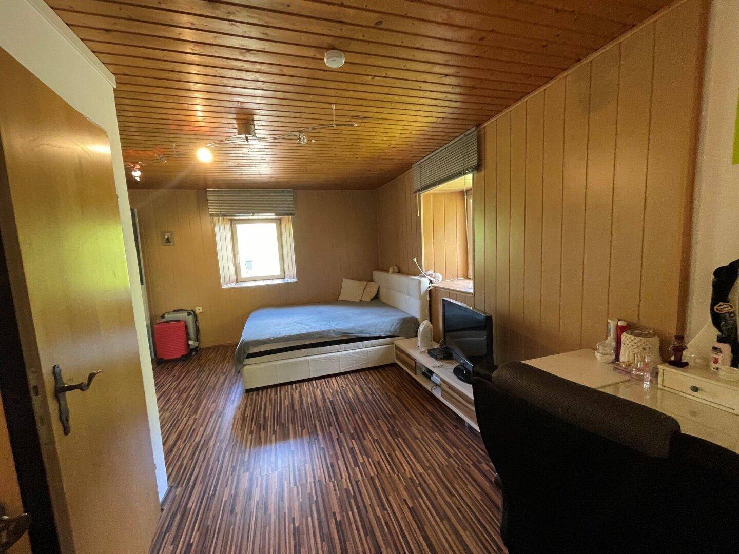 Schlafzimmer mit Holzwänden, Holzdecke, Laminatboden und Doppelbett.