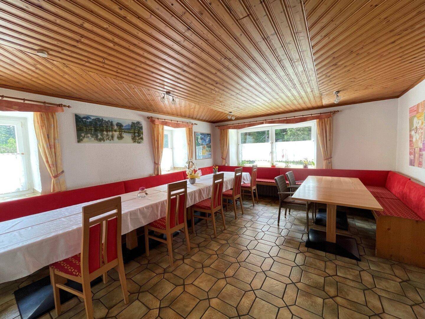 Geräumiger Speisesaal mit Holztischen, roten Sitzbänken und Fliesenboden.