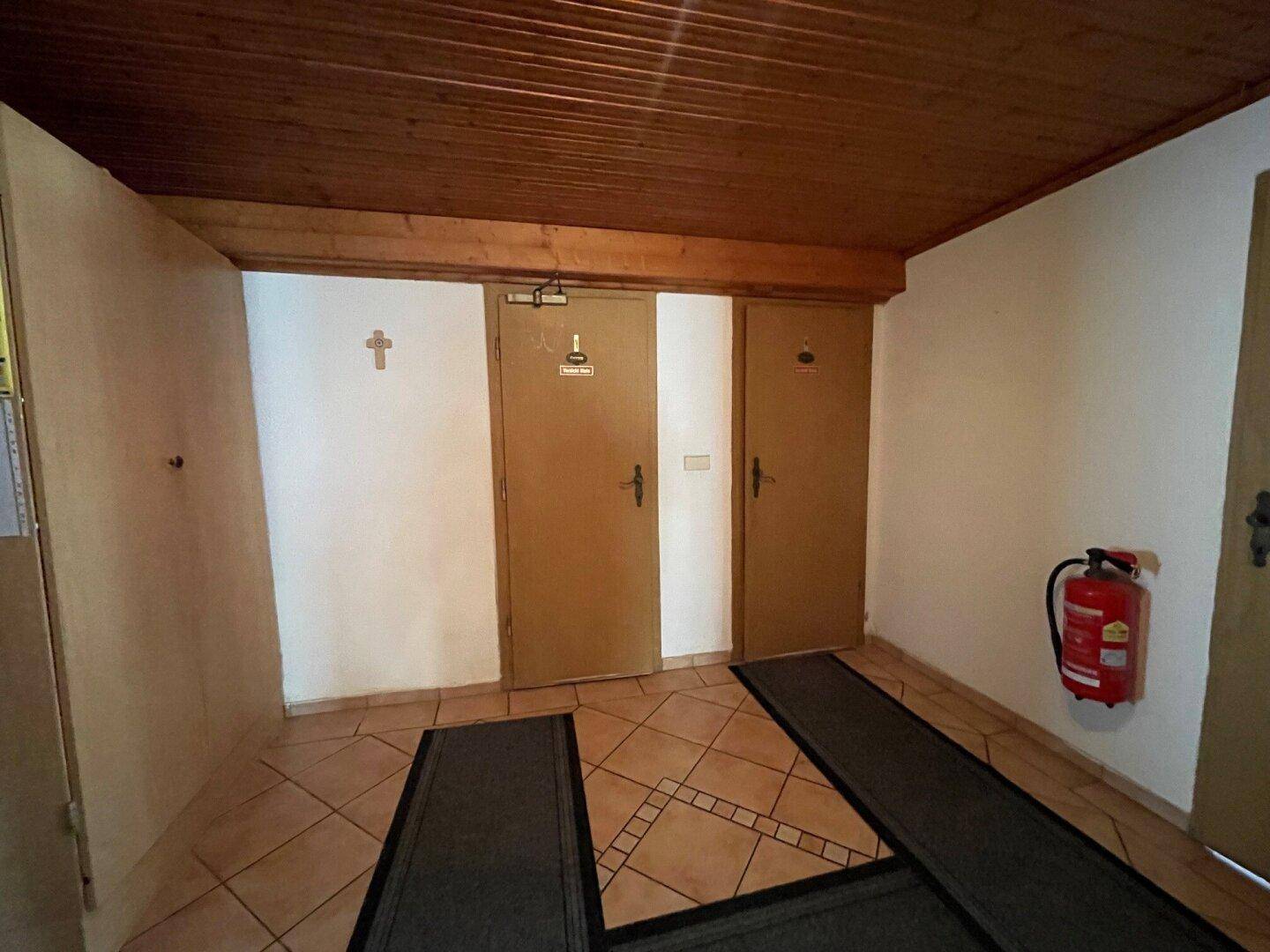 Flur mit Zugang zu den Toiletten und einem Feuerlöscher an der Wand.