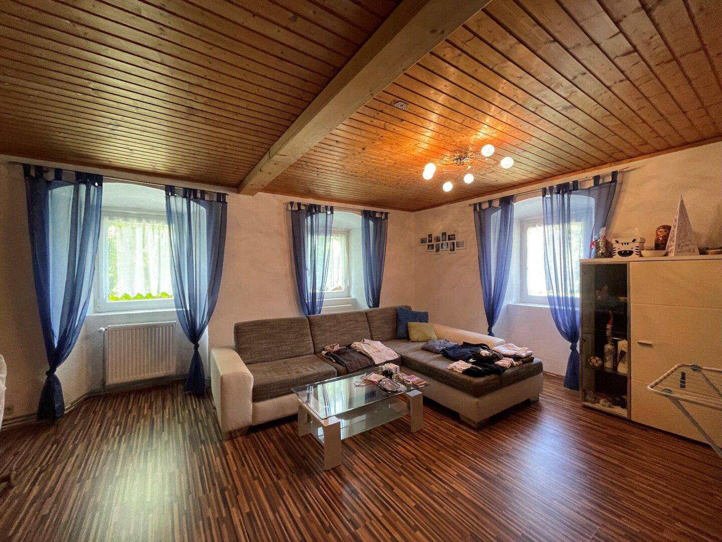 Gemütliches Wohnzimmer mit Holzboden, Holzdecke und blauen Vorhängen.