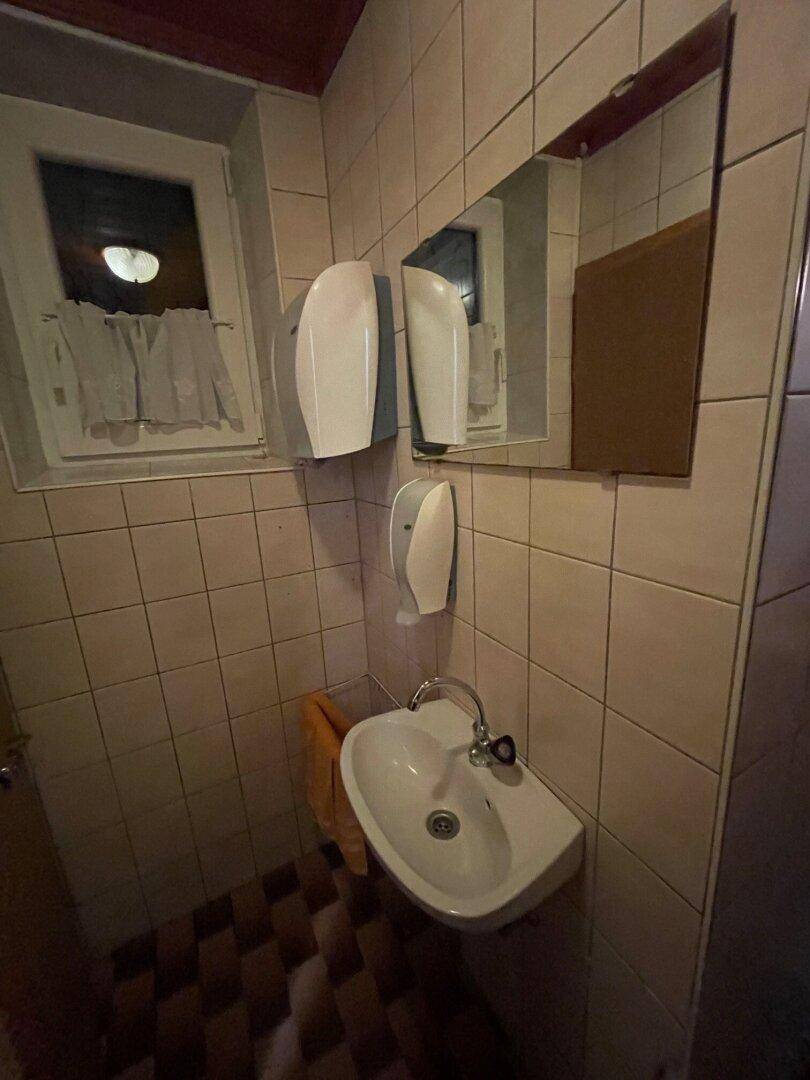 Kleiner Waschraum mit Fliesenwänden, Einzelwaschbecken und Fenster.