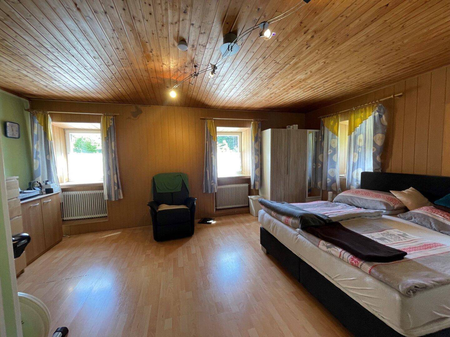 Helles Schlafzimmer mit Holzboden, Holzdecke und großem Bett.