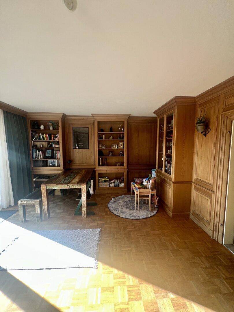 Geräumiges Wohnzimmer mit warmem Holzinterieur, Parkettboden und viel Tageslicht durch große Fenster.