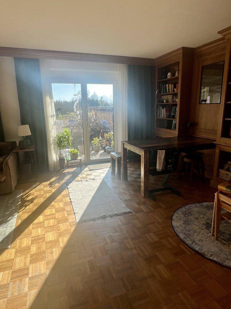 Helles Wohnzimmer mit Eichenparkett, maßgefertigten Holzregalen und Zugang zu einem sonnigen Außenbereich.