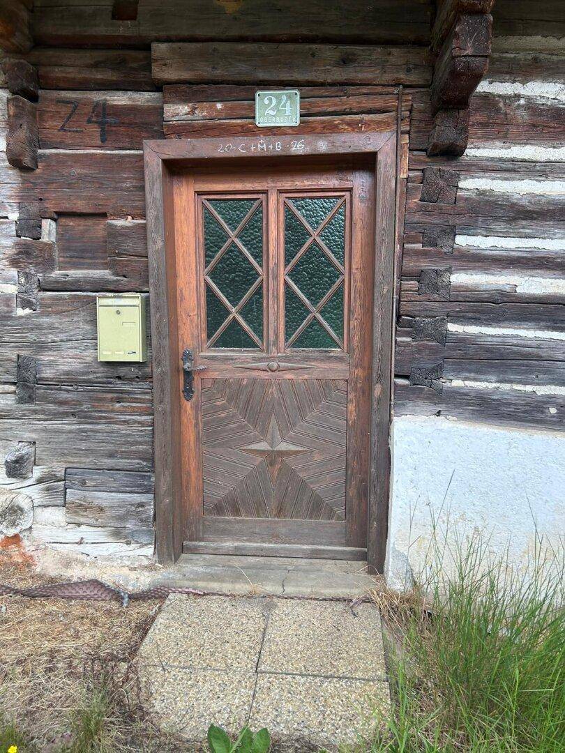 Alter Holzeingang mit geschnitzter Tür und Hausnummer 24 an der Fassade eines rustikalen Holzhauses.