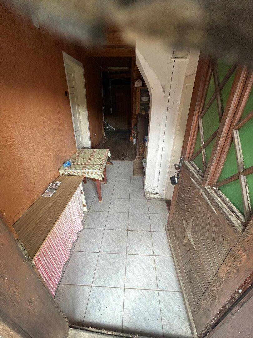 Schmaler Eingangsbereich mit Fliesenboden und Holztür, der zu weiteren Räumen im rustikalen Haus führt.