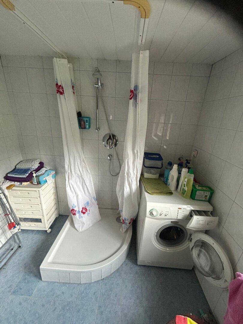 Funktionales Badezimmer mit Duschkabine, Waschmaschine und hellen Wandfliesen, praktisch und einfach.