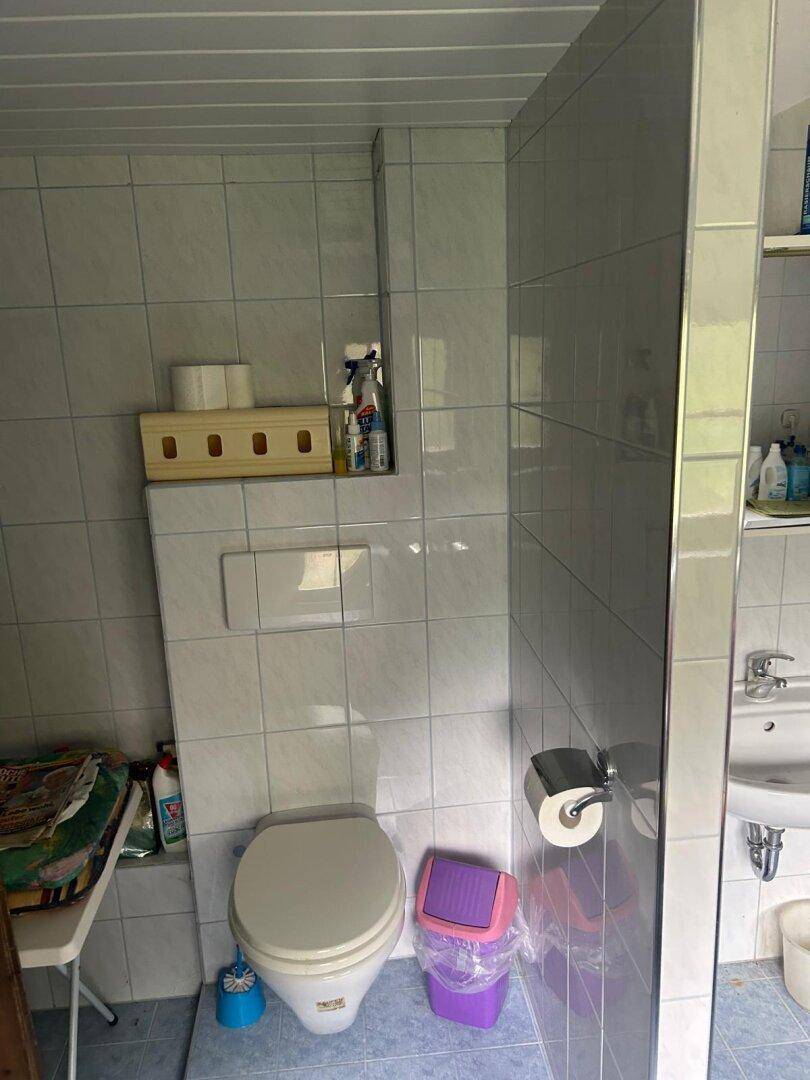Kleines WC mit Wand-WC und hellen Fliesen, integriert in ein Badezimmer mit einfacher Ausstattung.