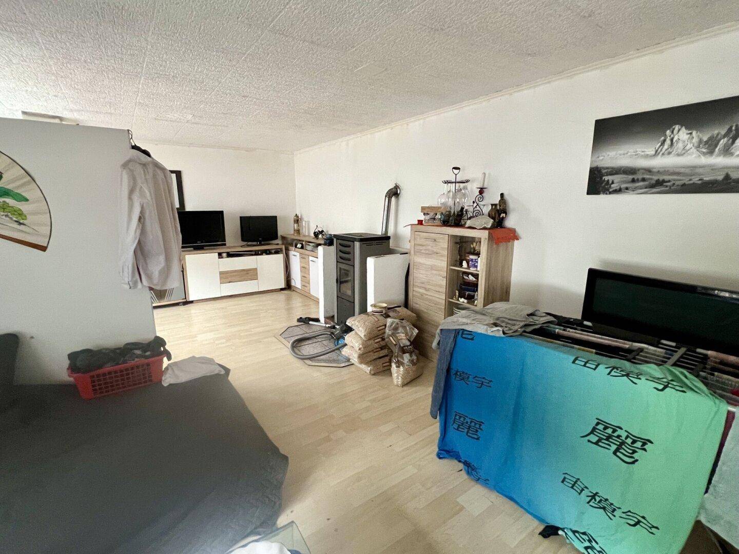 Geräumiges Wohnzimmer mit hellem Laminatboden, Kaminofen und verschiedenen Möbelstücken.