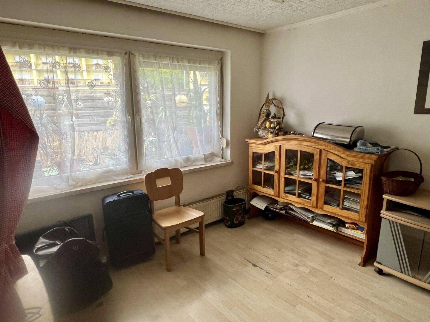 Heller Raum mit großen Fenstern, Laminatboden und einem Holzschrank mit Glasvitrine.