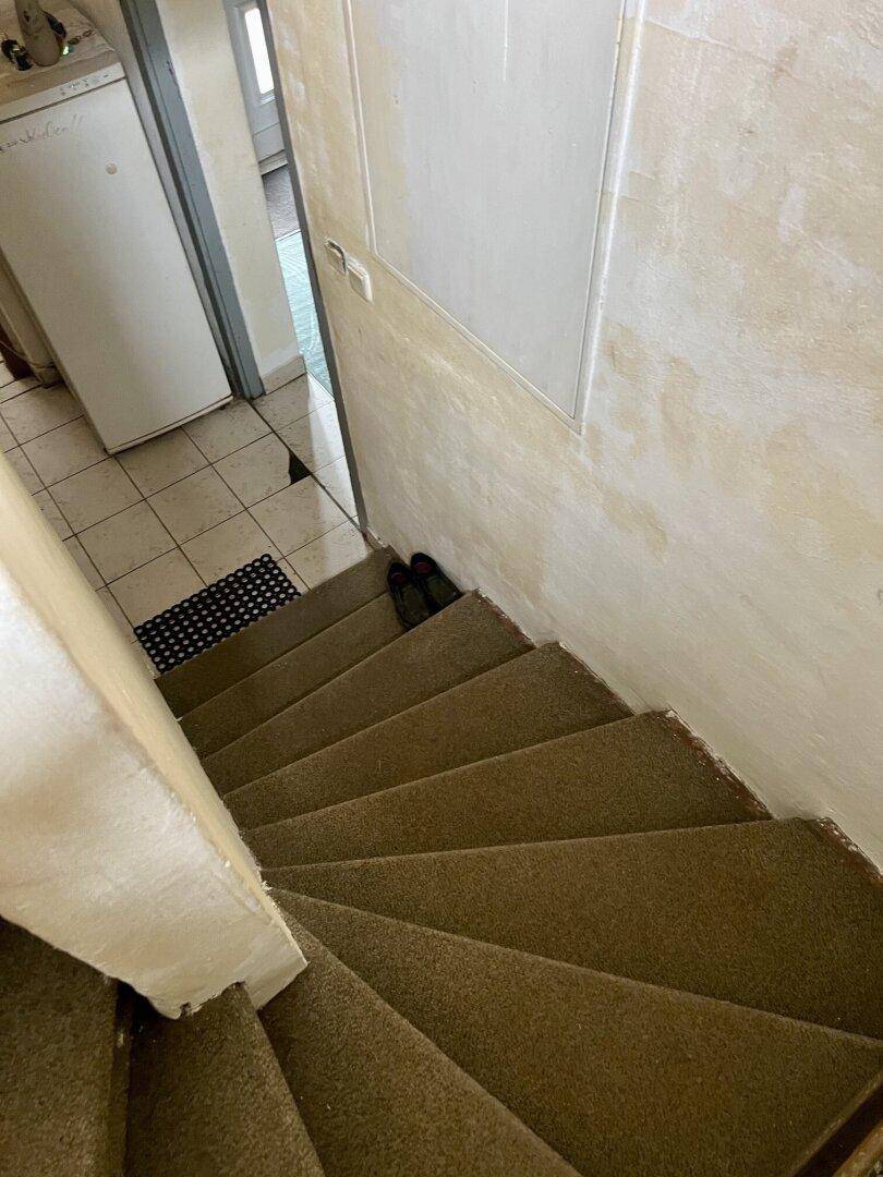 Treppenhaus mit Teppichboden, das in einen gefliesten Bereich führt.