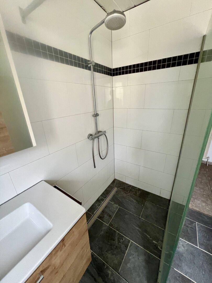 Modernisiertes Badezimmer mit ebenerdiger Dusche, Waschbecken und dunklen Fliesen.