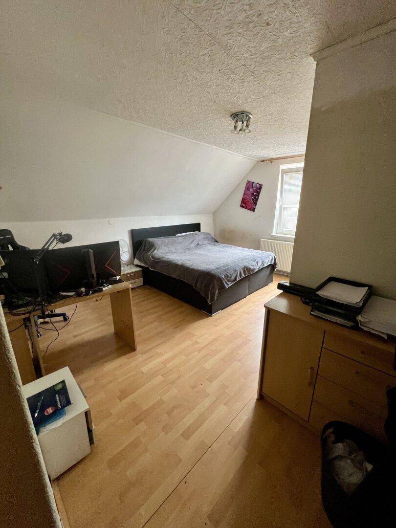 Schlafzimmer im Dachgeschoss mit schrägen Wänden, Laminatboden und einem Arbeitsbereich.