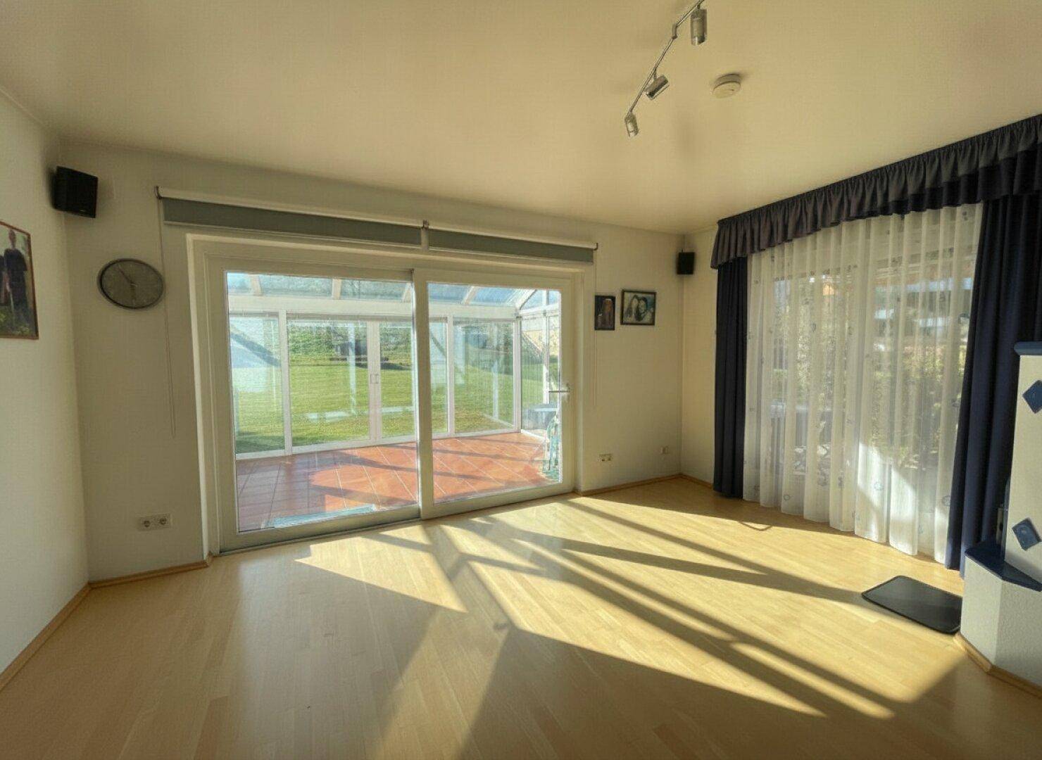 Helles Wohnzimmer mit Parkettboden, Zugang zum Wintergarten und traditionellem Kachelofen.