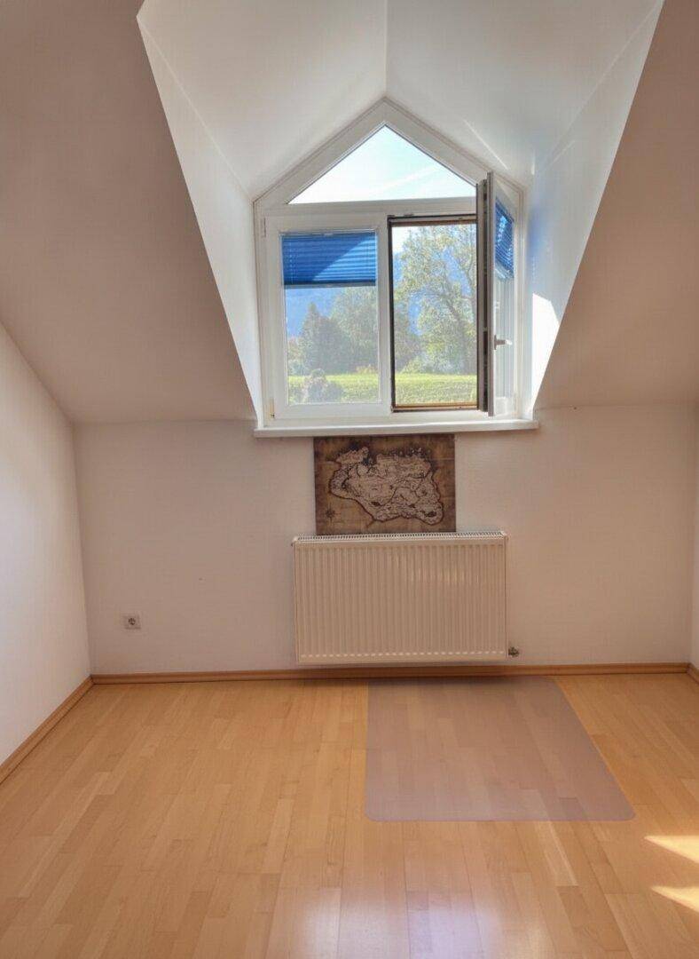 Helles Schlafzimmer mit Dachschräge, Holzparkettboden und Fenster mit Bergblick.
