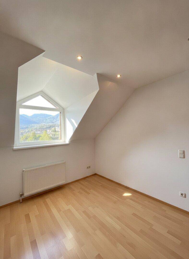 Schlafzimmer mit Dachschräge, Holzparkettboden und Fenster mit weitem Ausblick.