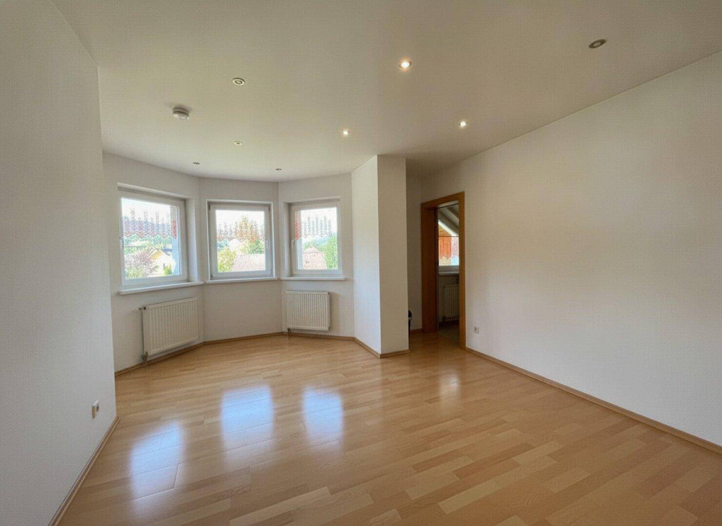 Geräumiger Raum mit Holzparkettboden, mehreren Fenstern und Einbaustrahlern an der Decke.