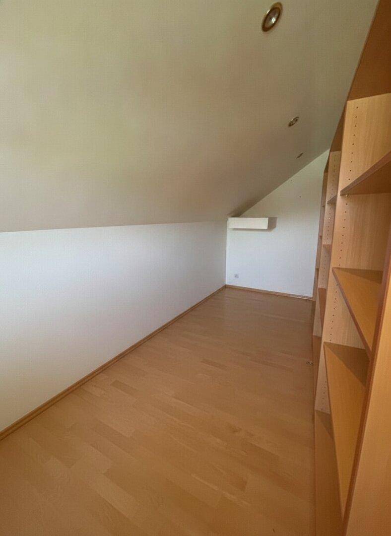 Dachgeschossraum mit schräger Decke, Holzparkettboden und eingebauten Regalen.