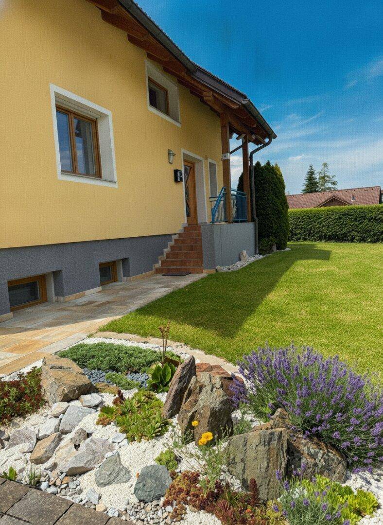 Gelbes Haus mit Steingarten, blühendem Lavendel und gepflegtem Rasen unter blauem Himmel.