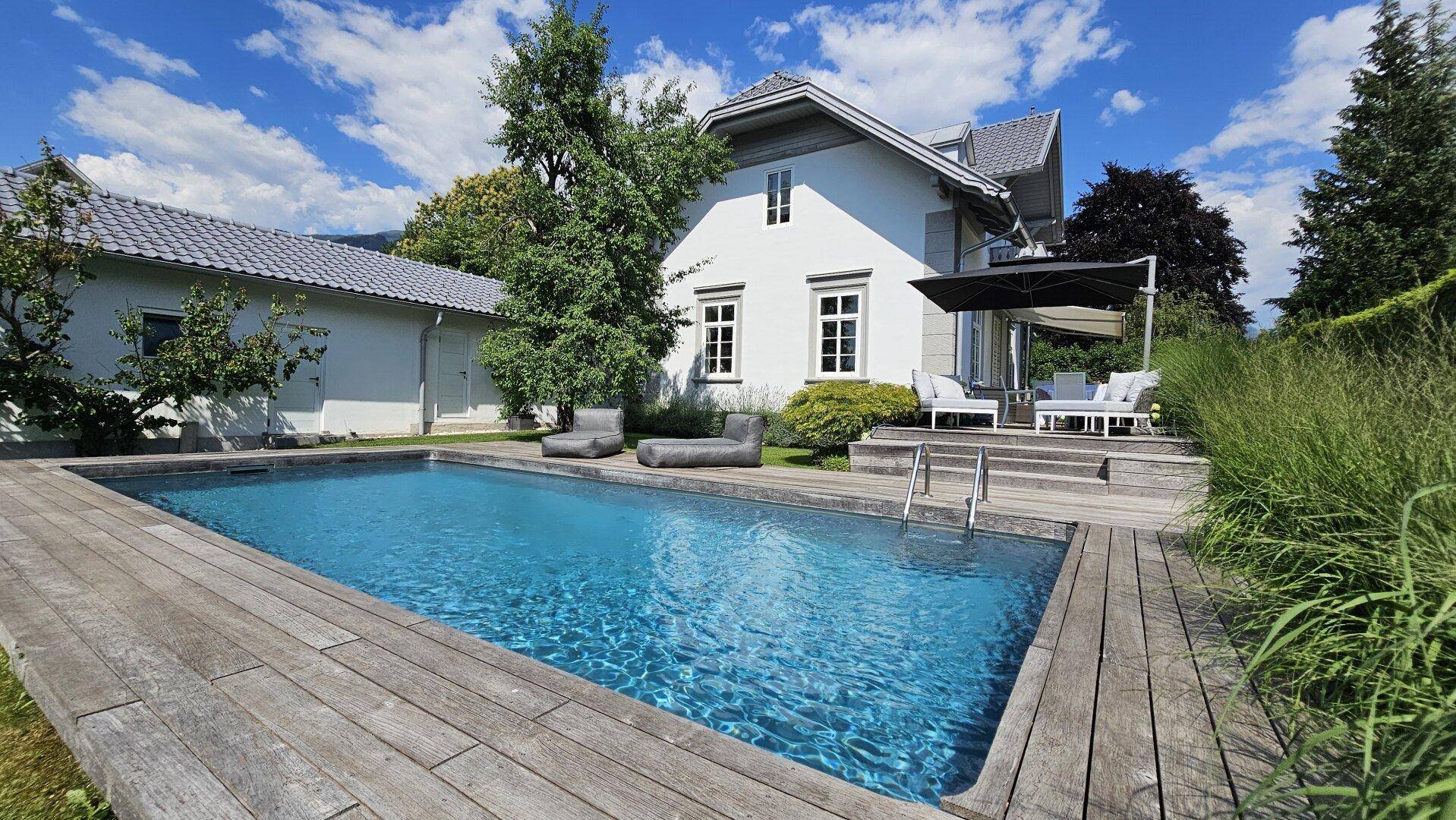 Idyllischer Garten mit erfrischendem Pool, umgeben von einem Holzdeck und einer sonnigen Terrasse am Haus.