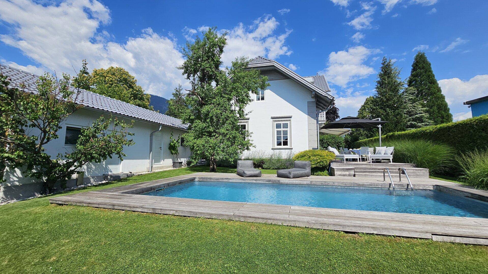 Gepflegter Garten mit Schwimmbecken, Holzumrandung und Liegeflächen, ideal für entspannte Sommertage.