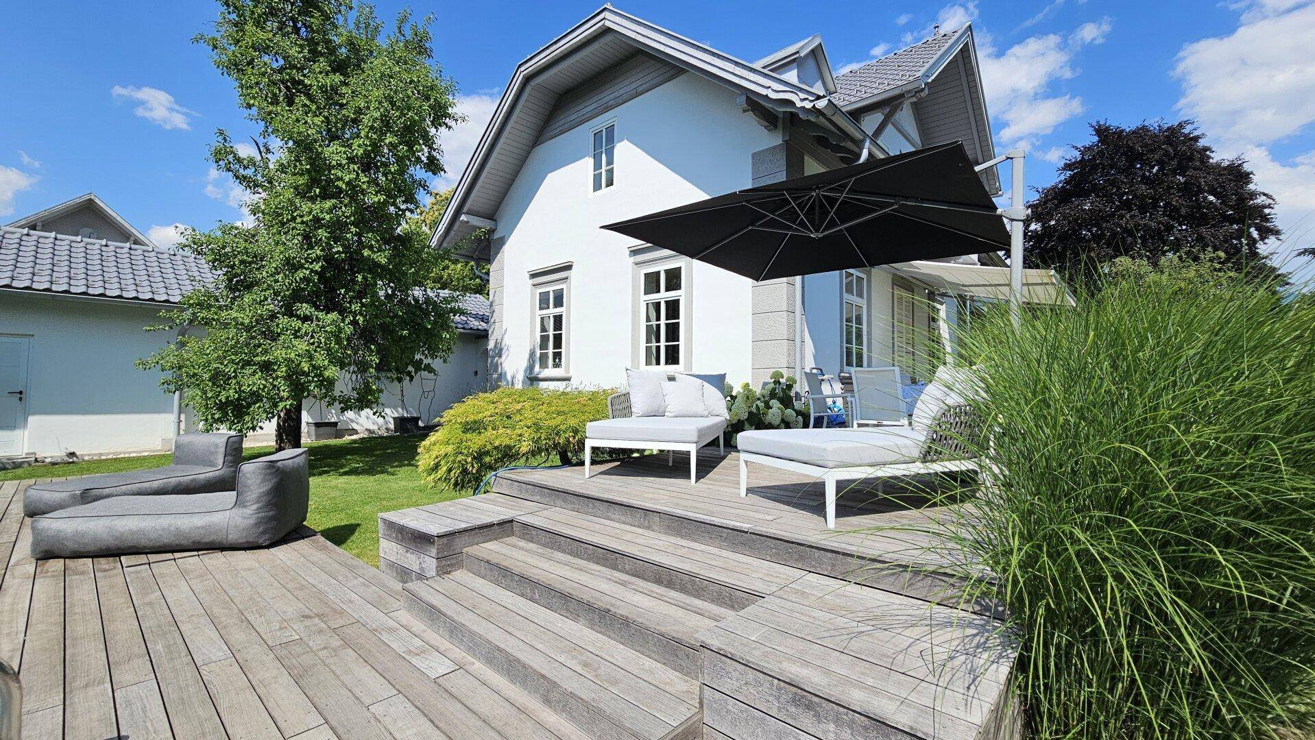 Stilvolle Holzterrasse mit modernen Lounge-Möbeln und großem Sonnenschirm, perfekt zum Entspannen im Freien.