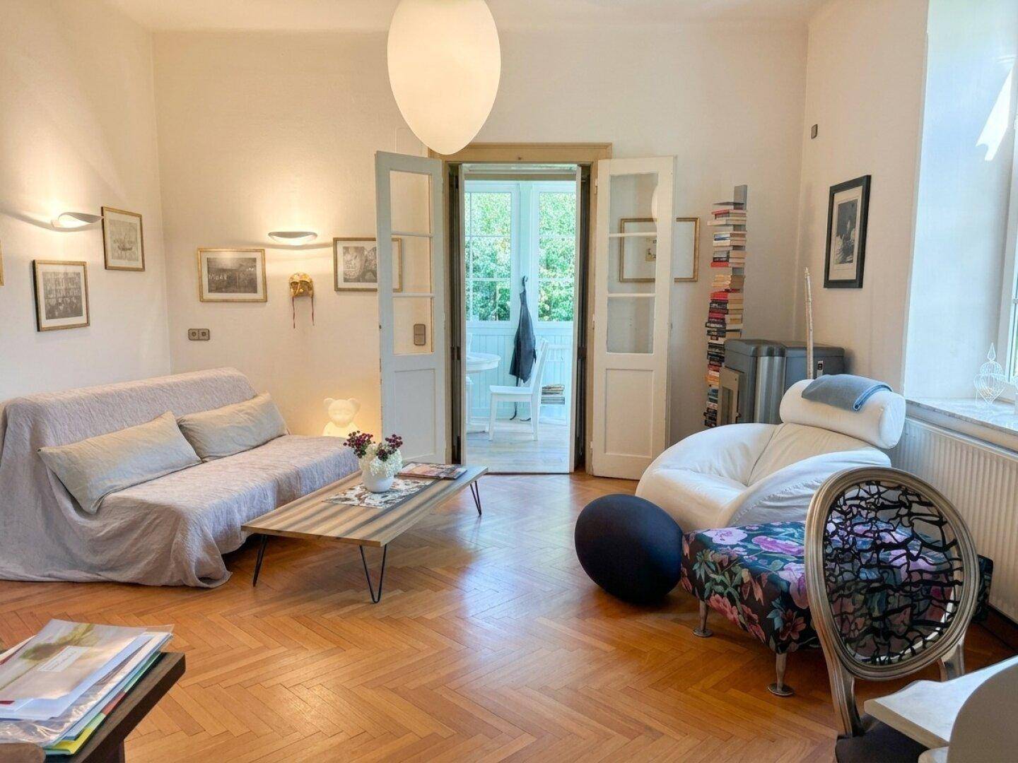 Helles Wohnzimmer mit bequemer Couch, Couchtisch und Flügeltüren, die zu einem weiteren Raum führen.