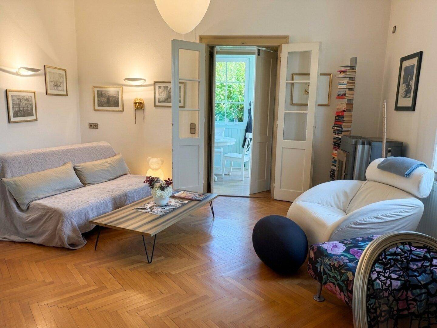 Einladendes Wohnzimmer mit klassischem Fischgrätparkett und stilvollen Möbeln, durch Flügeltüren verbunden.
