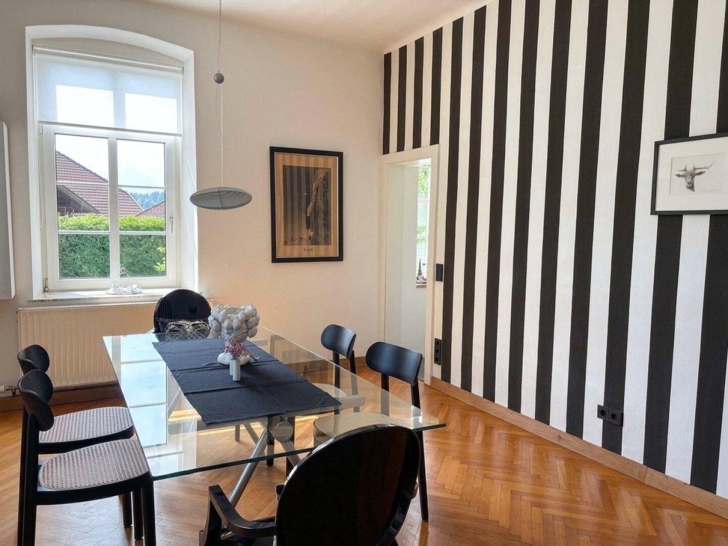 Modernes Esszimmer mit Glastisch, schwarzen Stühlen und einer auffälligen schwarz-weiß gestreiften Akzentwand.